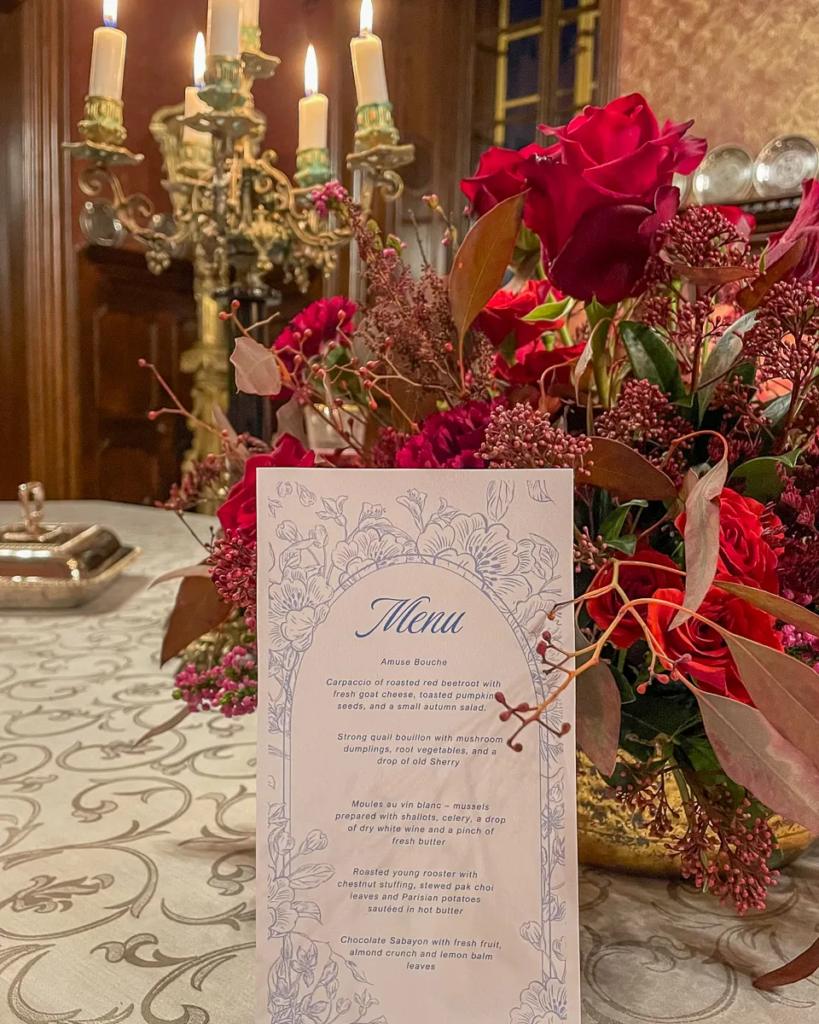 Printed autumn dinner menu standing among red flowers and candlelight at Chateau Loucen.